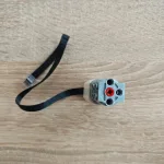Торцева частина сірого корпуса Мотора WeDo 2.0 з червоним отвором для валу та чорним шлейфом на дерев'яній поверхні