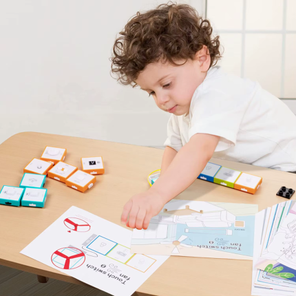 Дитина за столом збирає схему за допомогою електронних блоків та навчальних карток для керування вентилятором