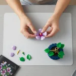 Процес конструювання гібіскуса: руки збирають фіолетове суцвіття над робочою поверхнею, поруч лежать окремі деталі листя та інструкція